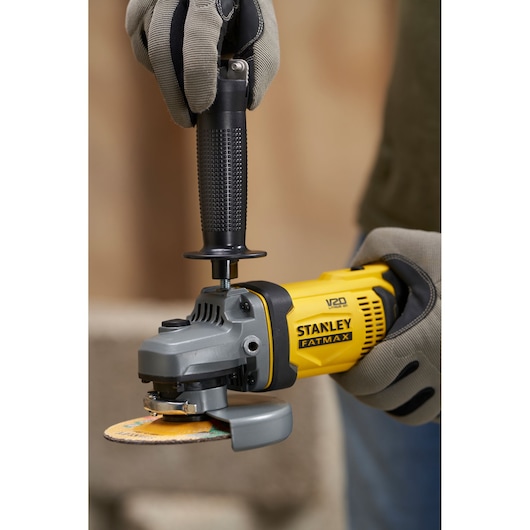 Photo of STANLEY SFMCG400M1K angle grinder in use, yellow and black body, with side handle, close-up view.