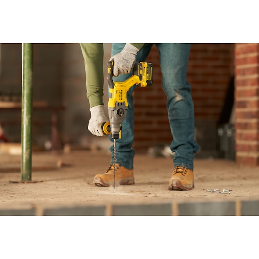 STANLEY SFMCH900M12 rotary hammer drill in use, worker drilling into concrete floor at construction site.