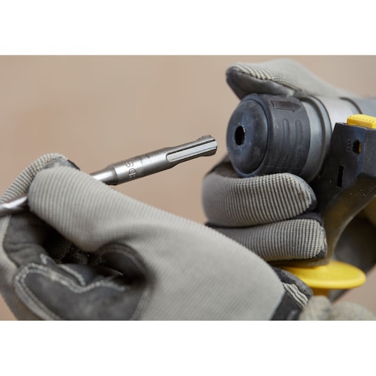 Photo of a gloved hand inserting a drill bit into a STANLEY SFMCH900M12 rotary hammer, close-up view.