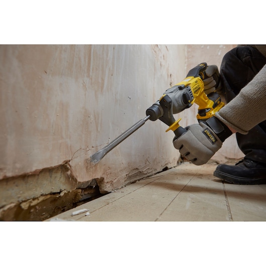 STANLEY SFMCH900M12 rotary hammer drilling into wall, close-up action shot, worker wearing gloves.
