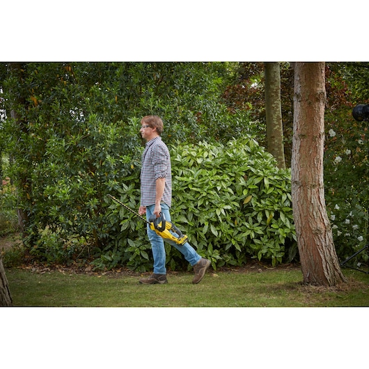 STANLEY SFMCHT855M1 hedge trimmer held by person walking outdoors, product in landscape use context.