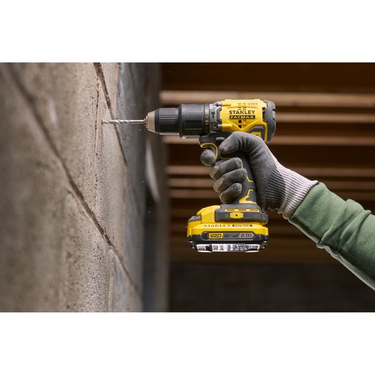 Photo of STANLEY SFMCK461D2S cordless drill in use drilling into a concrete wall, close-up of tool and gloved hand.