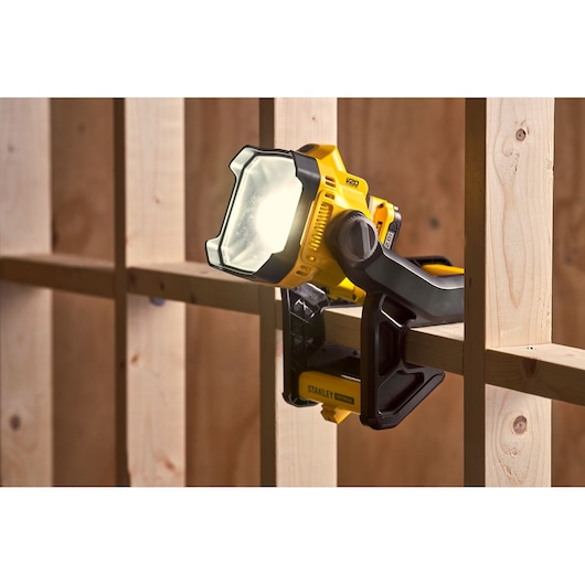 STANLEY SFMCL030B work light clamped to wooden beam, yellow and black, illuminated, side view.