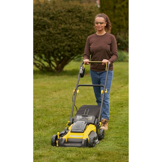 Photo of STANLEY SFMCMW2651M lawn mower with yellow and black design, being pushed on grass outdoors.