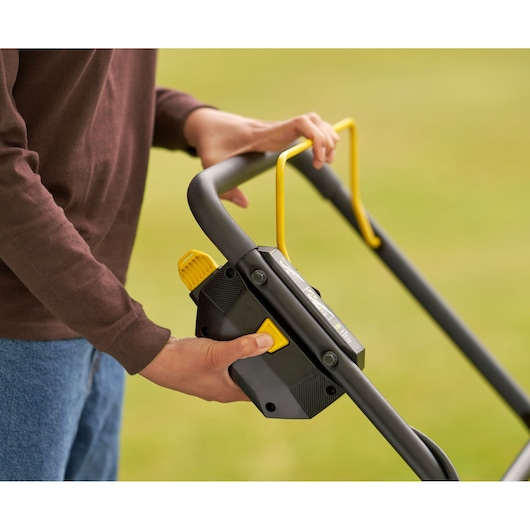 STANLEY SFMCMW2651M lawn mower handle close-up with yellow control lever and buttons outdoors.