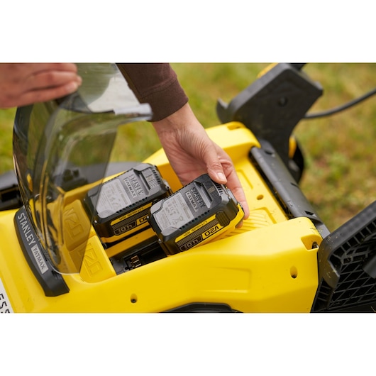 STANLEY SFMCMW2651M battery being inserted into yellow lawn mower, close-up outdoor view.