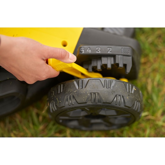 STANLEY SFMCMW2651M lawn mower height adjustment lever close-up with hand, grass background.