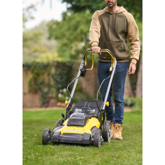 STANLEY SFMCMWS251M lawn mower with yellow and black body, shown in use on grass, front angle.
