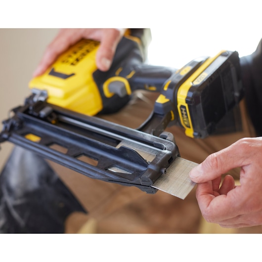 STANLEY SFMCN616B nailer photo, close-up of hand loading nails into yellow and black cordless tool.