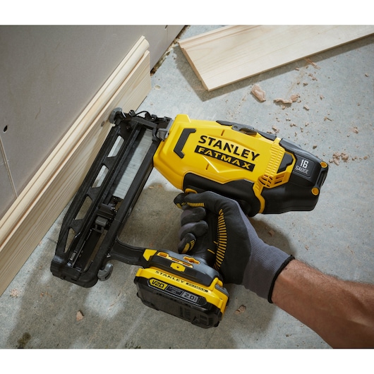 STANLEY SFMCN616D2K nail gun, yellow and black, used for wood baseboard installation, close-up.