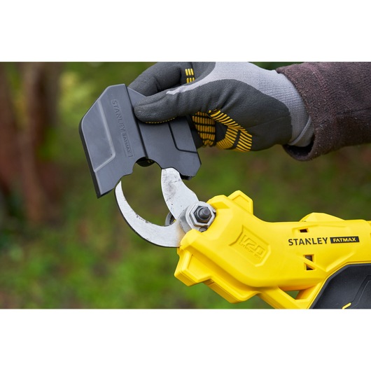 Photo of STANLEY SFMCPP32B garden pruner in yellow, close-up of gloved hand placing black blade cover outdoors.