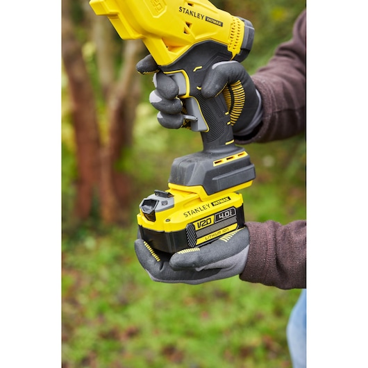 Photo of STANLEY SFMCPP32M1 cordless tool with V20 4.0Ah battery held outdoors by gloved hands.