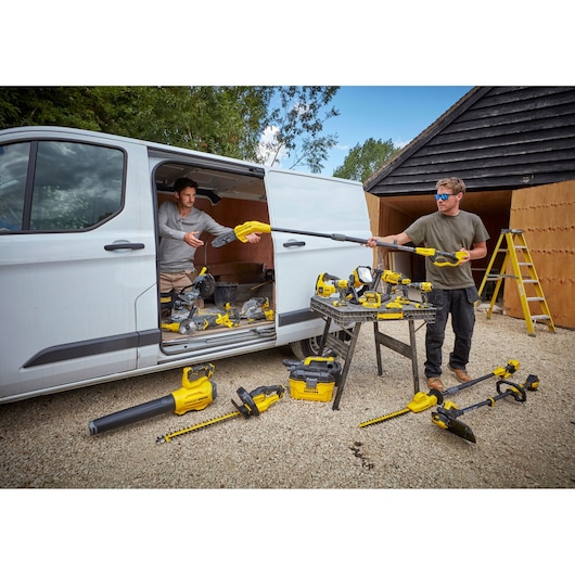 STANLEY SFMCPS620B power tools displayed outdoors with workers, van, and work table.