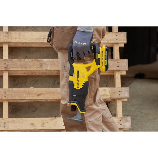 Stanley SFMCS300D1K yellow and black reciprocating saw held by gloved hand, shown outdoors near wooden pallets.