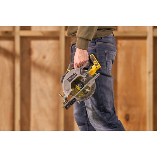 STANLEY SFMCS500M1K circular saw held by person in work clothes, workshop background.