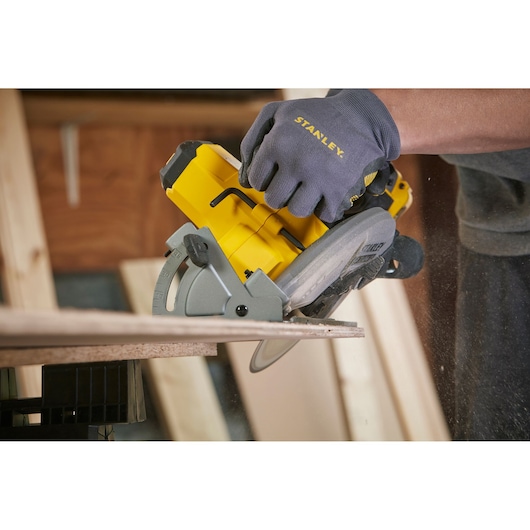 Photo of STANLEY SFMCS500M1K circular saw cutting wood, close-up with gloved hand in workshop.