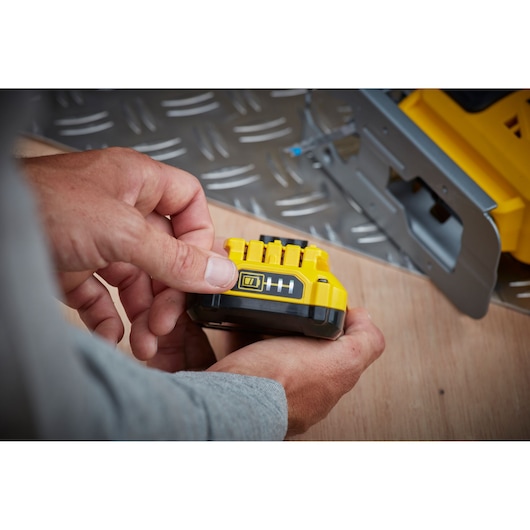 STANLEY SFMCS600D1K yellow battery held in hand, showing charge indicator, workshop background.