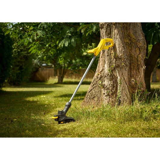 STANLEY SFMCST925M1 grass trimmer with yellow handle resting on tree in garden.