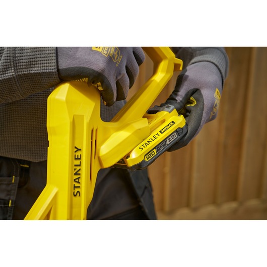 STANLEY SFMCST925M1 yellow cordless tool close-up, gloved hands inserting V20 battery.