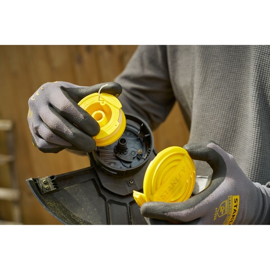STANLEY SFMCST925M1 spool replacement for string trimmer, close-up with yellow parts and gloves.