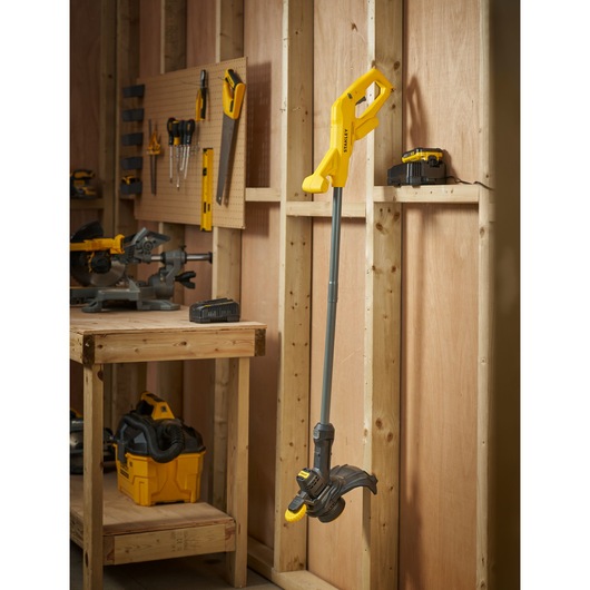 STANLEY SFMCST925M1 cordless string trimmer in yellow and black, side view, hanging in a workshop.