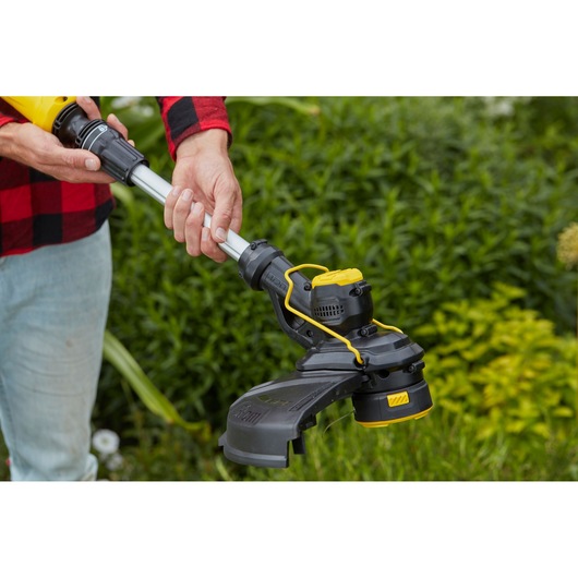 STANLEY SFMCST933M1 string trimmer held outdoors, close-up on handle and cutting head.
