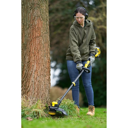 STANLEY SFMCSTB933M cordless string trimmer, yellow and black, used outdoors near tree.