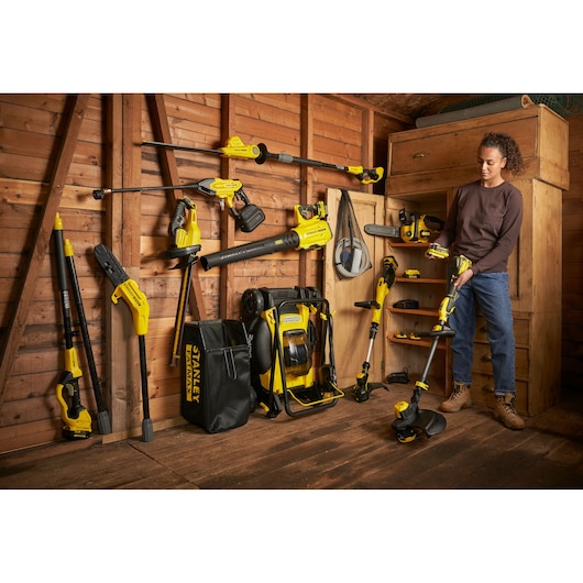 Photo of STANLEY SFMCSTB933M garden tools and accessories neatly arranged in a wooden shed, with person holding trimmer.