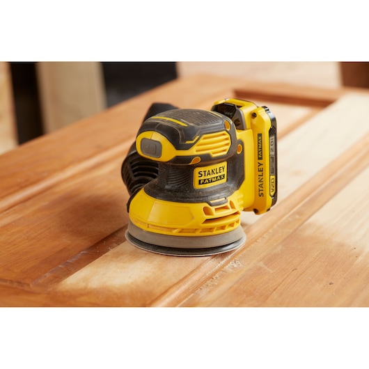 STANLEY SFMCW220B cordless sander on wooden surface, yellow and black, close-up side angle.