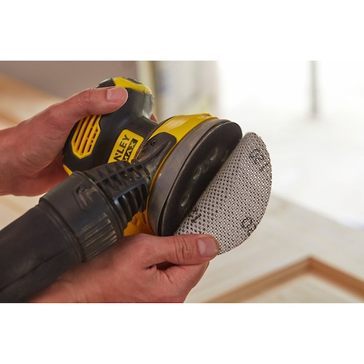 Photo of STANLEY SFMCW220B cordless sander held by hands, attaching mesh sanding pad.
