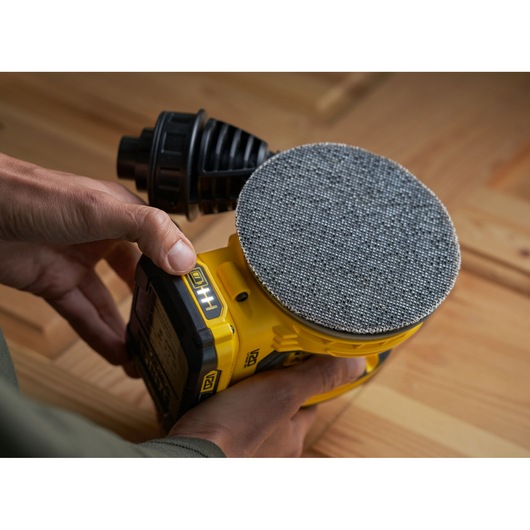 STANLEY SFMCW220B cordless sander held by hand, showing round sanding pad and yellow body.