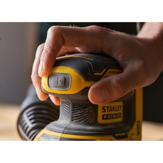 Photo of STANLEY SFMCW220D1S sander, handheld, yellow and black, close-up showing power button.