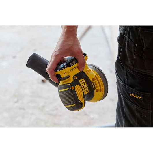 Photo of STANLEY SFMCW220D1S cordless random orbital sander in hand, yellow and black color.