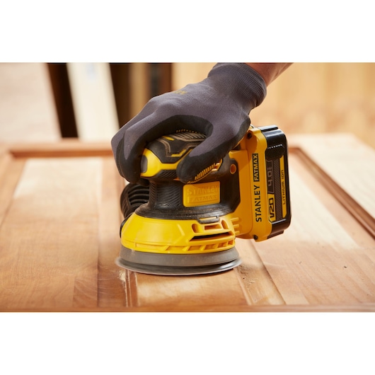 Photo of STANLEY SFMCW220M1S cordless sander in use on wooden surface, close-up angle.