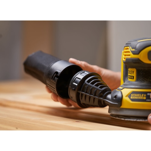 STANLEY SFMCW220M1S cordless sander close-up with dust collector detached, shown on wooden surface.