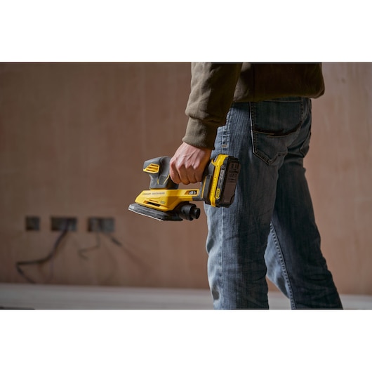 Photo of STANLEY SFMCW221B cordless sander held by a person in a workwear setting.
