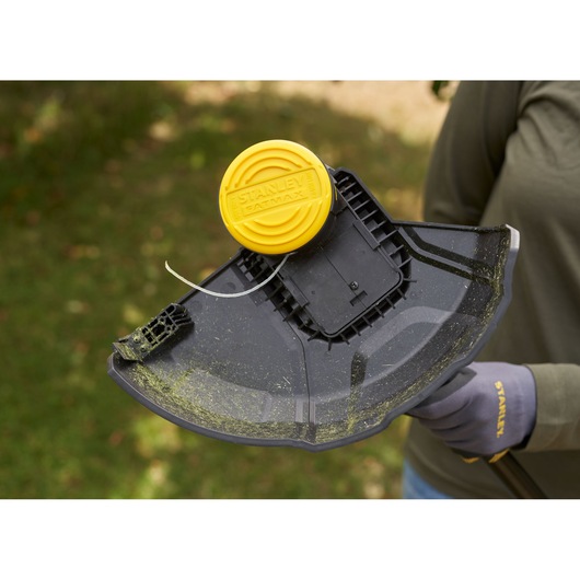Photo of STANLEY SFMSTB930M grass trimmer head with yellow cap and black shield, shown outdoors in use.