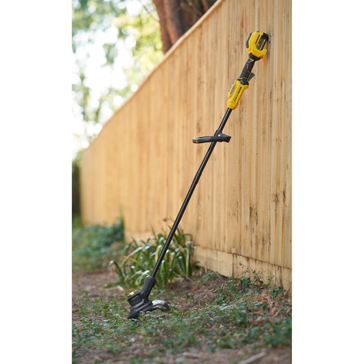 STANLEY SFMSTB930M grass trimmer in yellow and black leaning against a wooden fence outdoors.