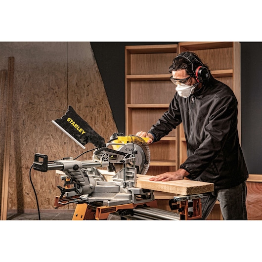 Photo of STANLEY SM18-B2C compound miter saw in use, cutting wood on a workbench in a workshop setting.