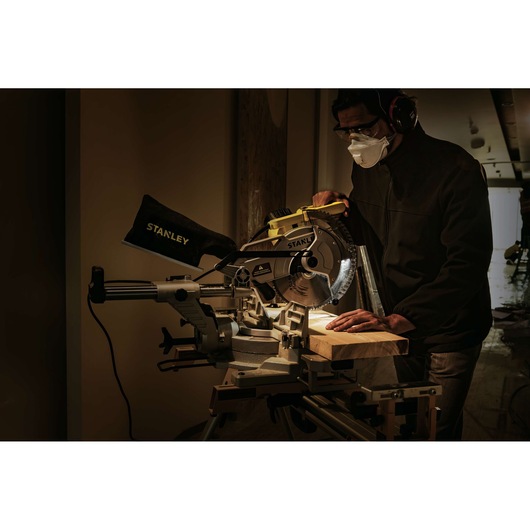 STANLEY SM18-B2C sliding miter saw in use cutting wood, operator wearing safety gear, workshop scene.