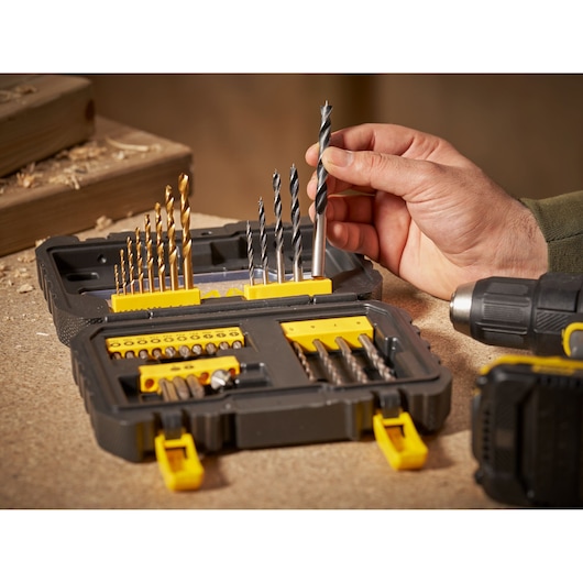 STANLEY STA88550 drill bit and accessory set open on workbench, hand selecting a drill bit, side angle.