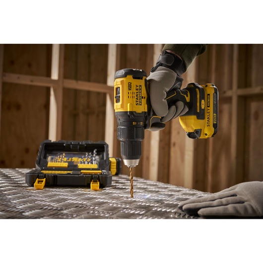 Stanley STA88550 cordless drill in use, yellow and black, with drill bit kit, workshop background.