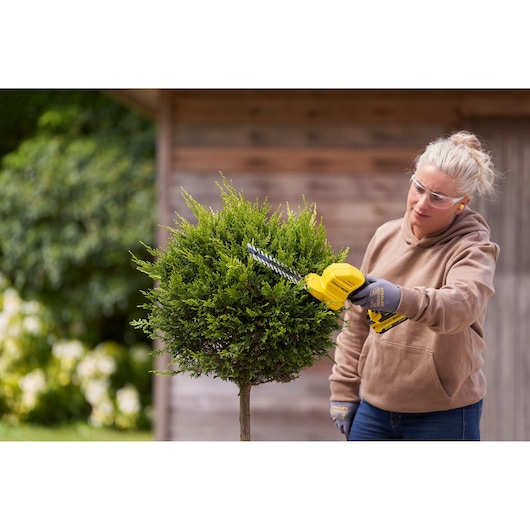 Photo of STANLEY STCSS20D1 hedge trimmer in use, trimming a green bush outdoors.