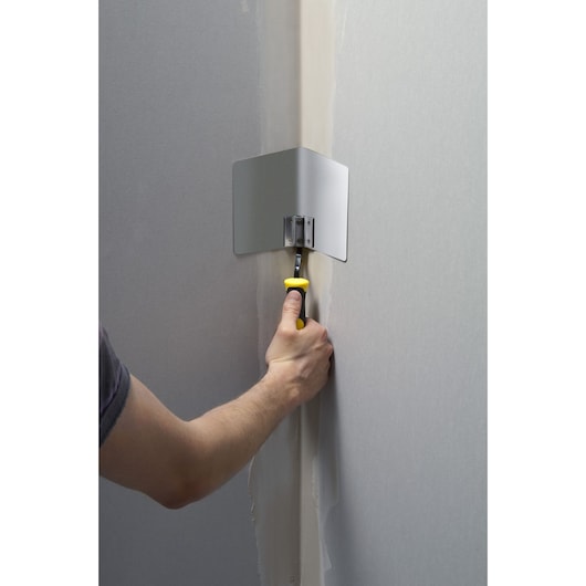 STANLEY STHT0-05777 corner finishing tool with yellow handle used to smooth joint compound in a wall corner.
