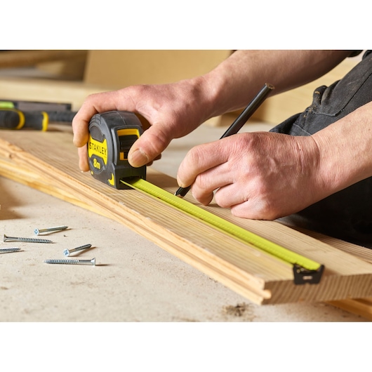 STANLEY STHT0-33566 tape measure in use marking wood, photo of product and hands in workshop setting.