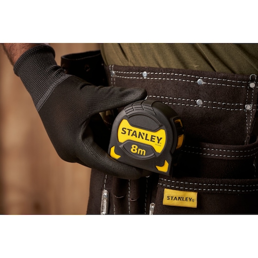 STANLEY STHT0-33566 8m tape measure held by gloved hand, shown in tool belt pouch, close-up view.