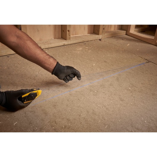 Photo of STANLEY STHT0-47147 chalk line tool in use, marking a straight blue line on a wooden floor.