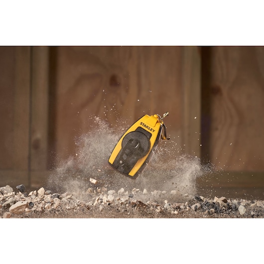 STANLEY STHT0-47147 chalk line in yellow and black, shown kicking up dust on rocky ground, action shot.