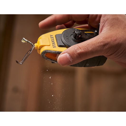 STANLEY STHT0-47147 chalk line reel in yellow and black held in a hand with chalk dust in midair.