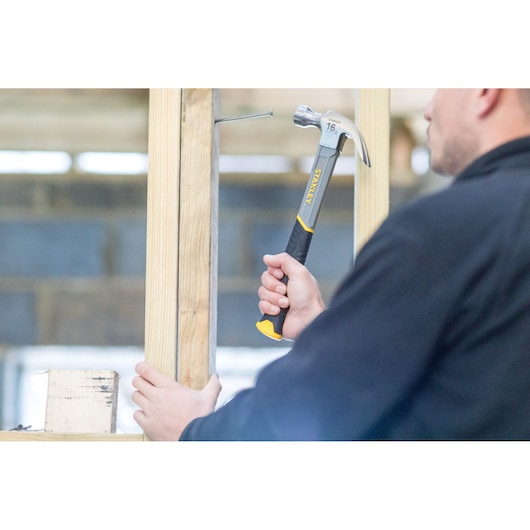 Person using STANLEY STHT0-51310 claw hammer on wood frame, close-up photo of tool handle and head.